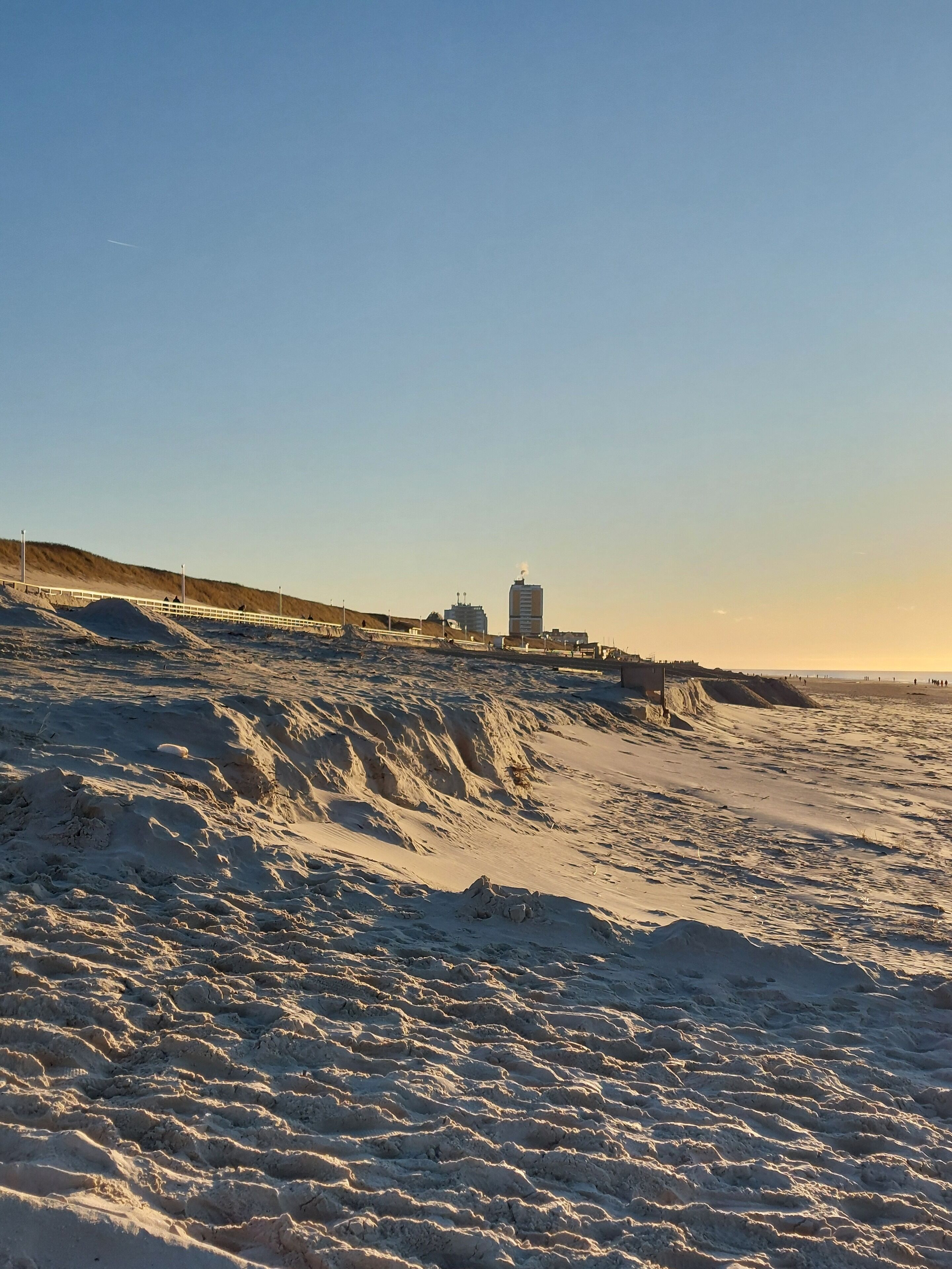 Ein Sandstrand mit einem weißen Zaun und einem Gebäude im Hintergrund.
