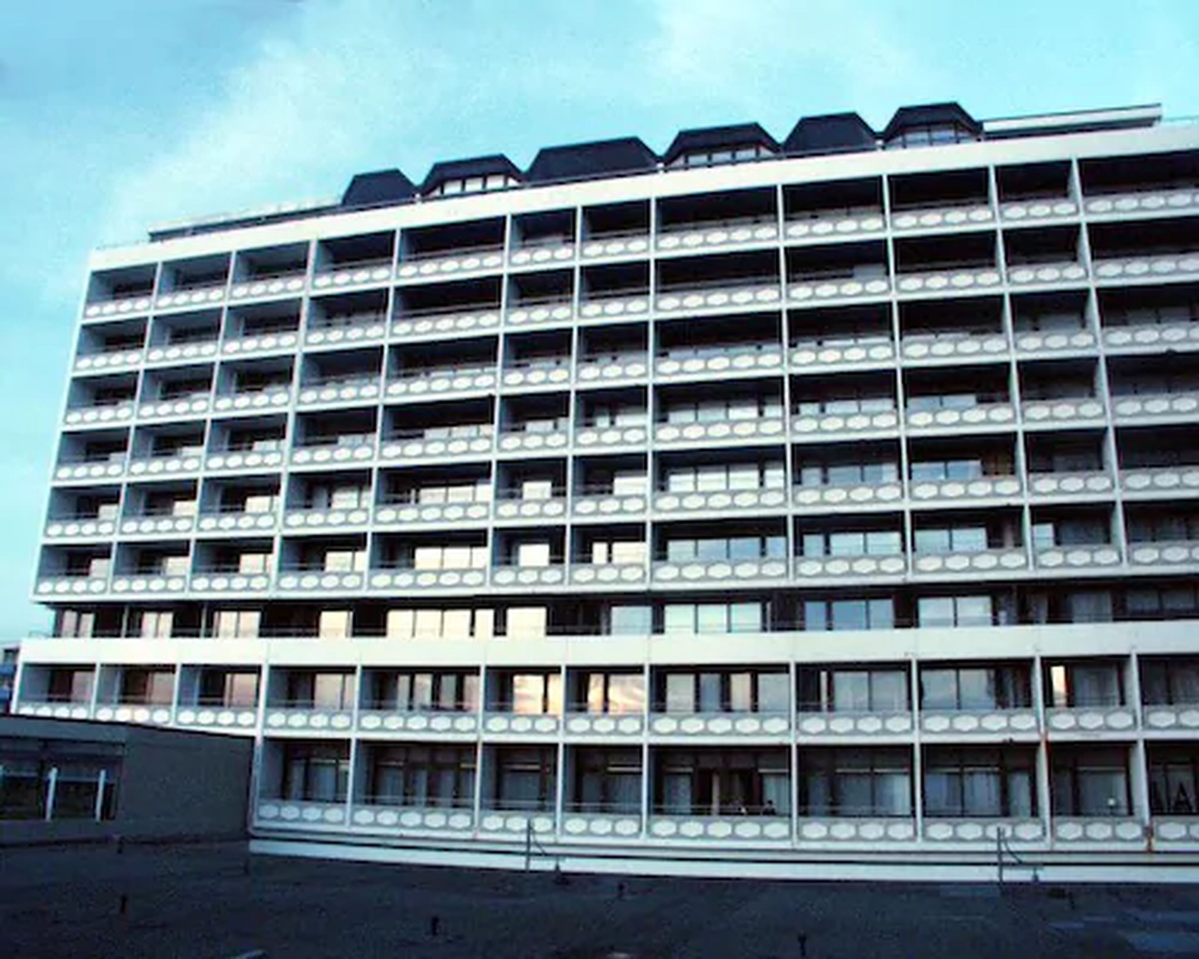 Un hotel a più piani con facciata uniforme, caratterizzato da balconi su ogni piano e un tetto piatto.
