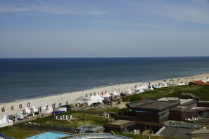 A coastal hotel with a swimming pool, beach tents, and a view of the ocean. - TOP CountryLine Hotel Roth am Strande (Sylt)