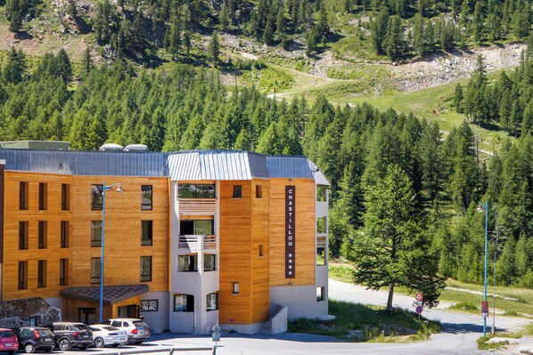 Ett hotell med flera våningar, en träfasad, en balkong på andra våningen och en bergskedja i bakgrunden.
