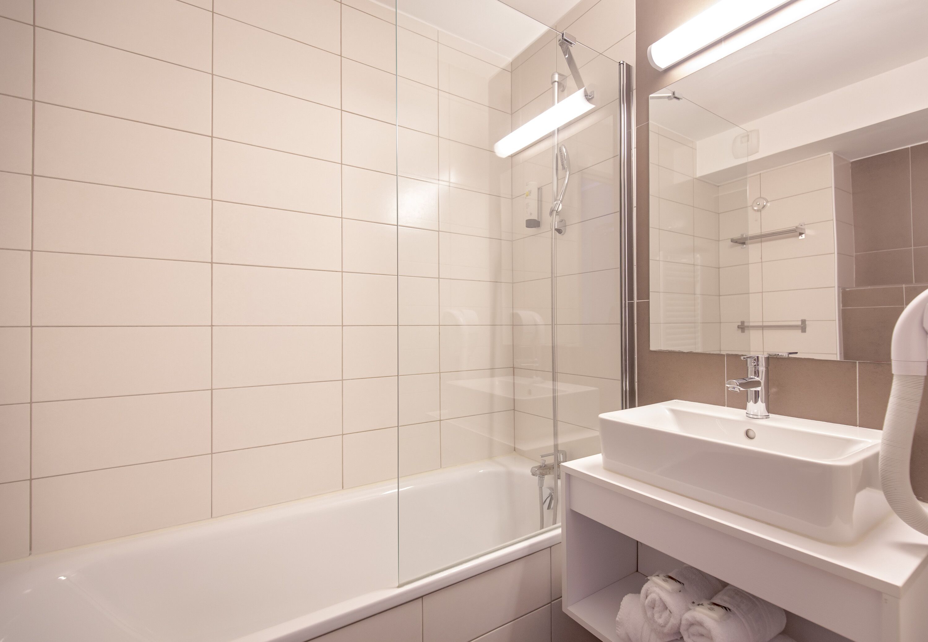 Ein modernes Badezimmer mit einer gläsernen Dusche, einer weißen Badewanne und einem Waschbecken mit Spiegel.