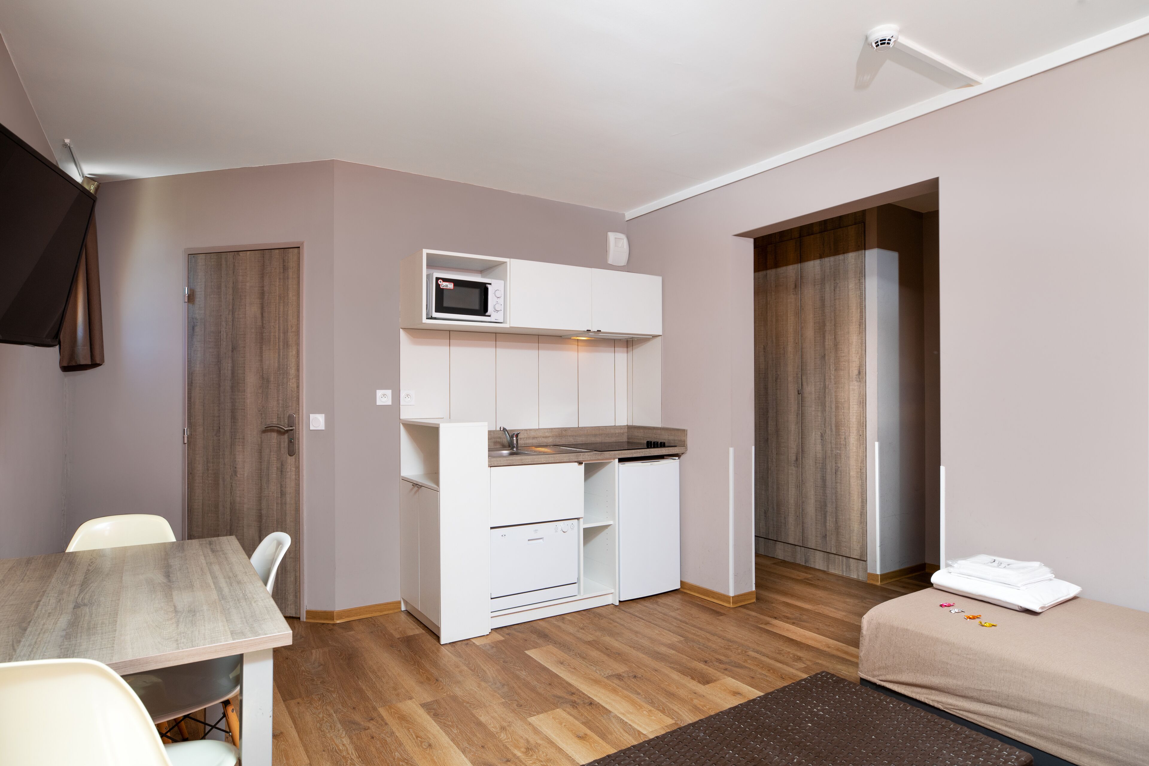 A compact room with a kitchenette, a dining area, and a bed.