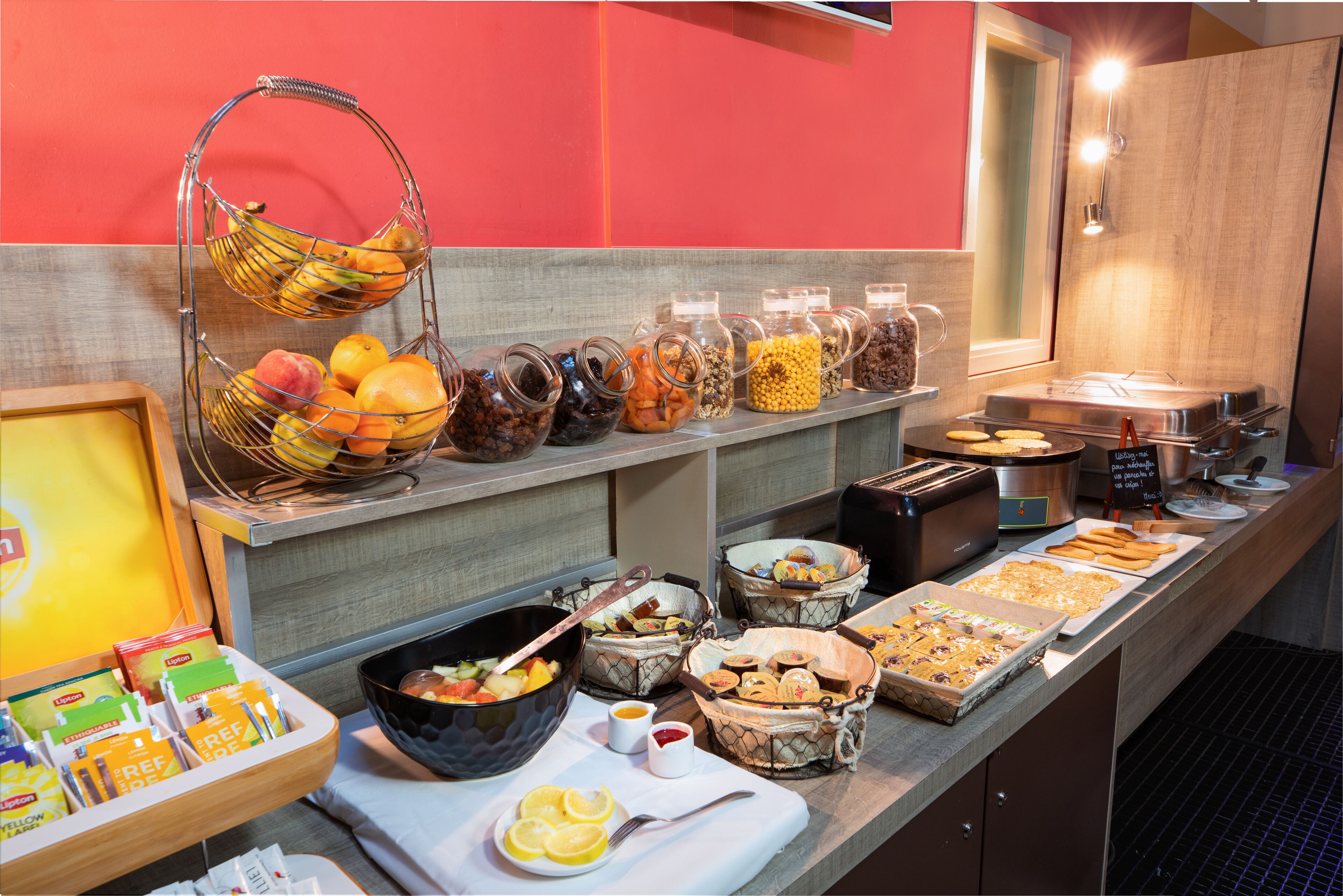 Un bufé con diversos alimentos, entre ellos frutas, cereales y productos de pastelería, dispuesto en un mostrador.