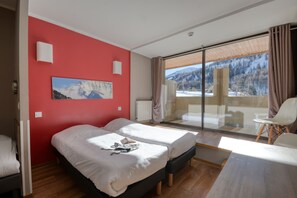 Ett hotellrum med två sängar, ett stort fönster med utsikt över bergen, en skjutdörr i glas och en vit stol.
