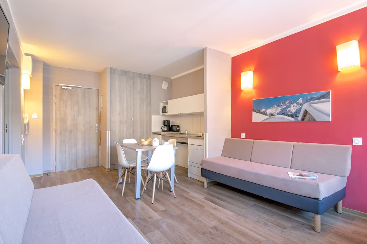Un espace de vie moderne et compact comprenant un coin cuisine, un coin repas et un espace détente avec un canapé et des fauteuils.