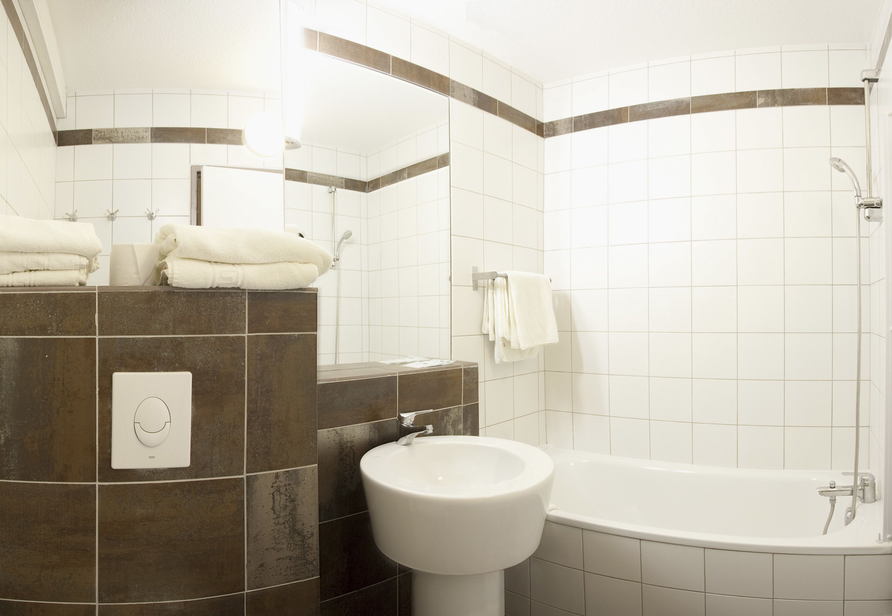 A bathroom with a bathtub, a sink, and a mirror. There are towels stacked on the counter.