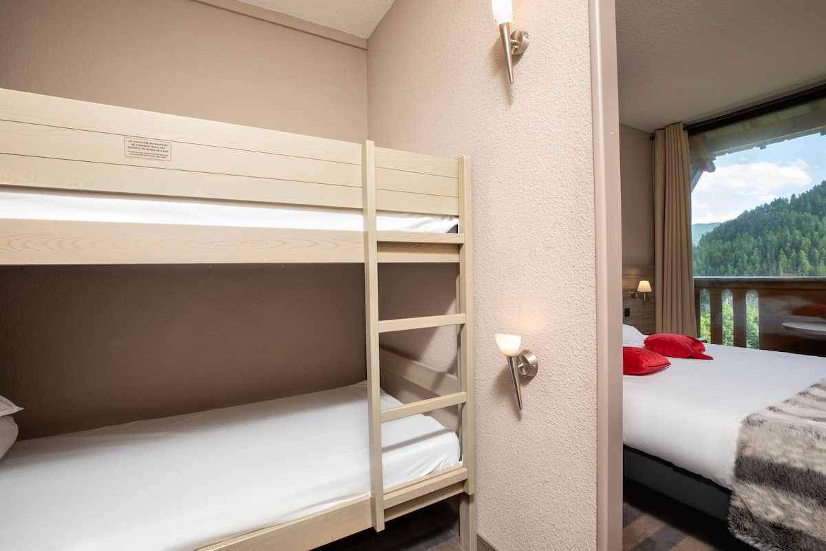 Une chambre avec des lits superposés donnant sur une colline boisée.