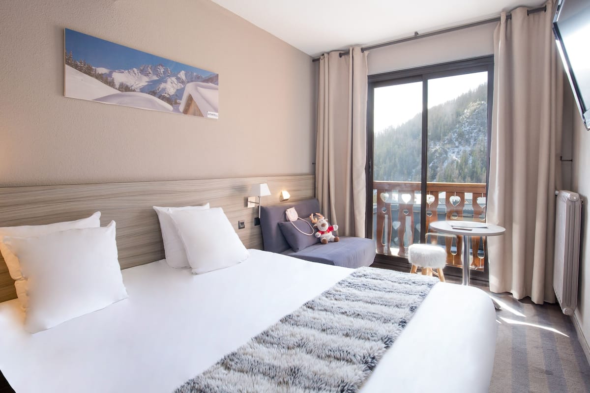 Une chambre d’hôtel avec un grand lit, un petit canapé, une table ronde et un balcon offrant une vue sur les montagnes.