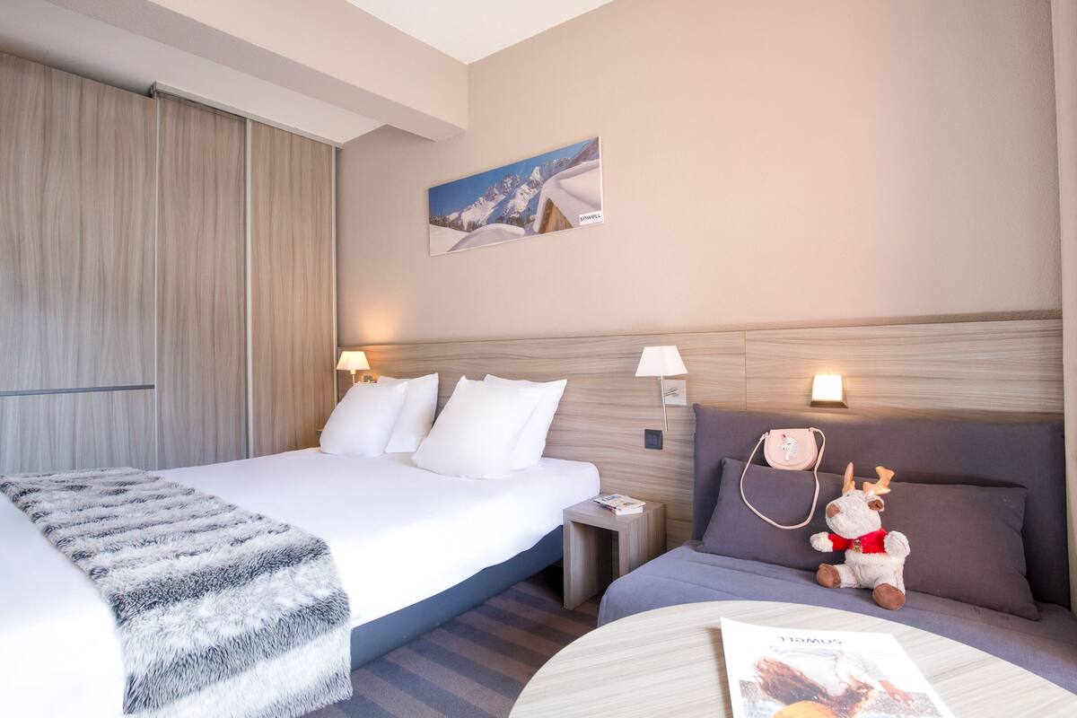 Une chambre d’hôtel avec un grand lit, une table de chevet, un canapé, un jouet en peluche et une lampe fixée au mur.