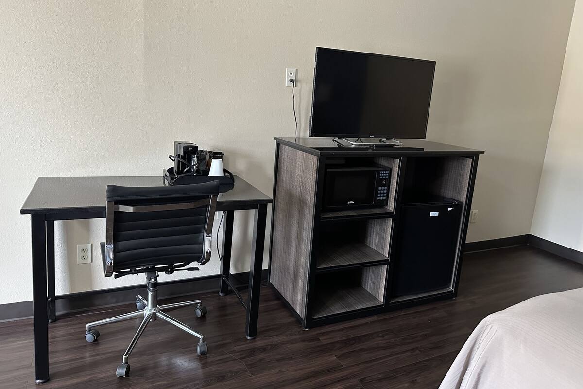 A hotel room with a desk, chair, and a flat-screen TV on a stand.
