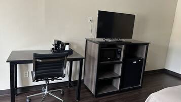 A hotel room with a desk, chair, and a flat-screen TV on a stand.