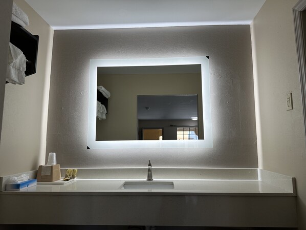 A bathroom with a large mirror, a sink, and a towel rack.