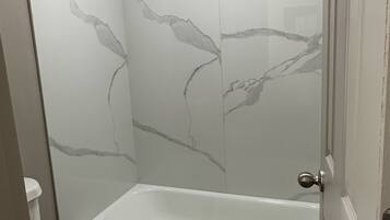 A bathroom with a bathtub, toilet, and a shower area with a glass door.