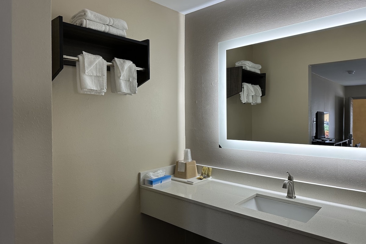 A bathroom with a sink, mirror, towel rack, and a bottle of hand soap.