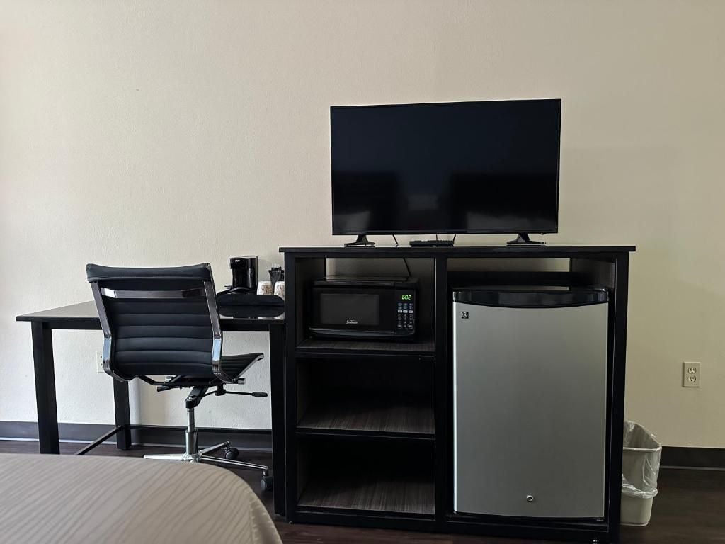 A hotel room with a bed, a desk with a computer, a television, a microwave, and a mini-fridge.