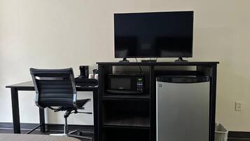 A hotel room with a bed, a desk with a computer, a television, a microwave, and a mini-fridge.