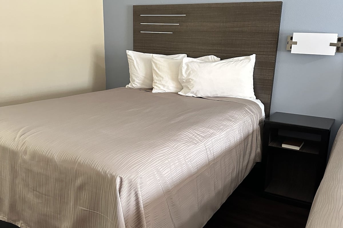 A neatly made bed with a headboard, a bedside table with a book, and a wall-mounted light fixture.