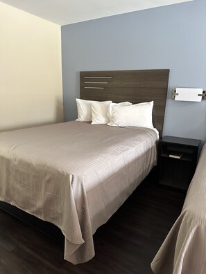 A neatly made bed with a headboard, a bedside table with a book, and a wall-mounted light fixture.