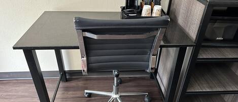 A black office chair with a high backrest and a metal base, positioned on a dark wooden floor.
