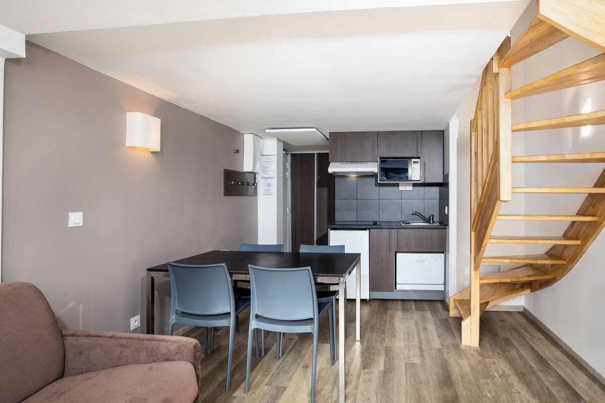 A modern kitchen with dark cabinets, a wooden staircase, and a dining area with a table and chairs.