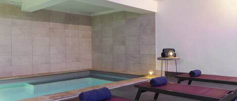 A spa area with a swimming pool, lounge chairs, and a massage table.