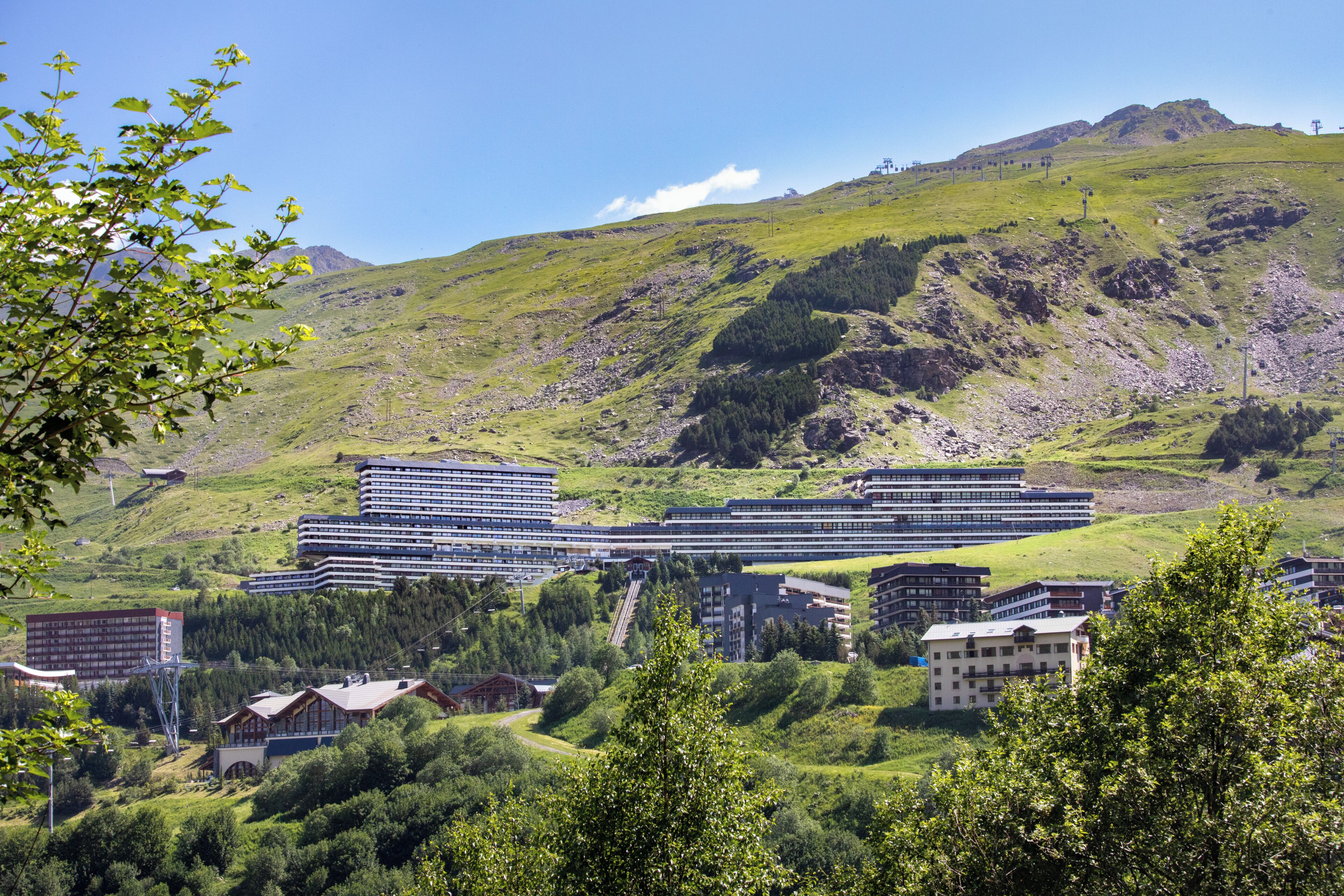 Ett modernt hotellkomplex med flera byggnader, omgivet av frodig grönska och kullar.
