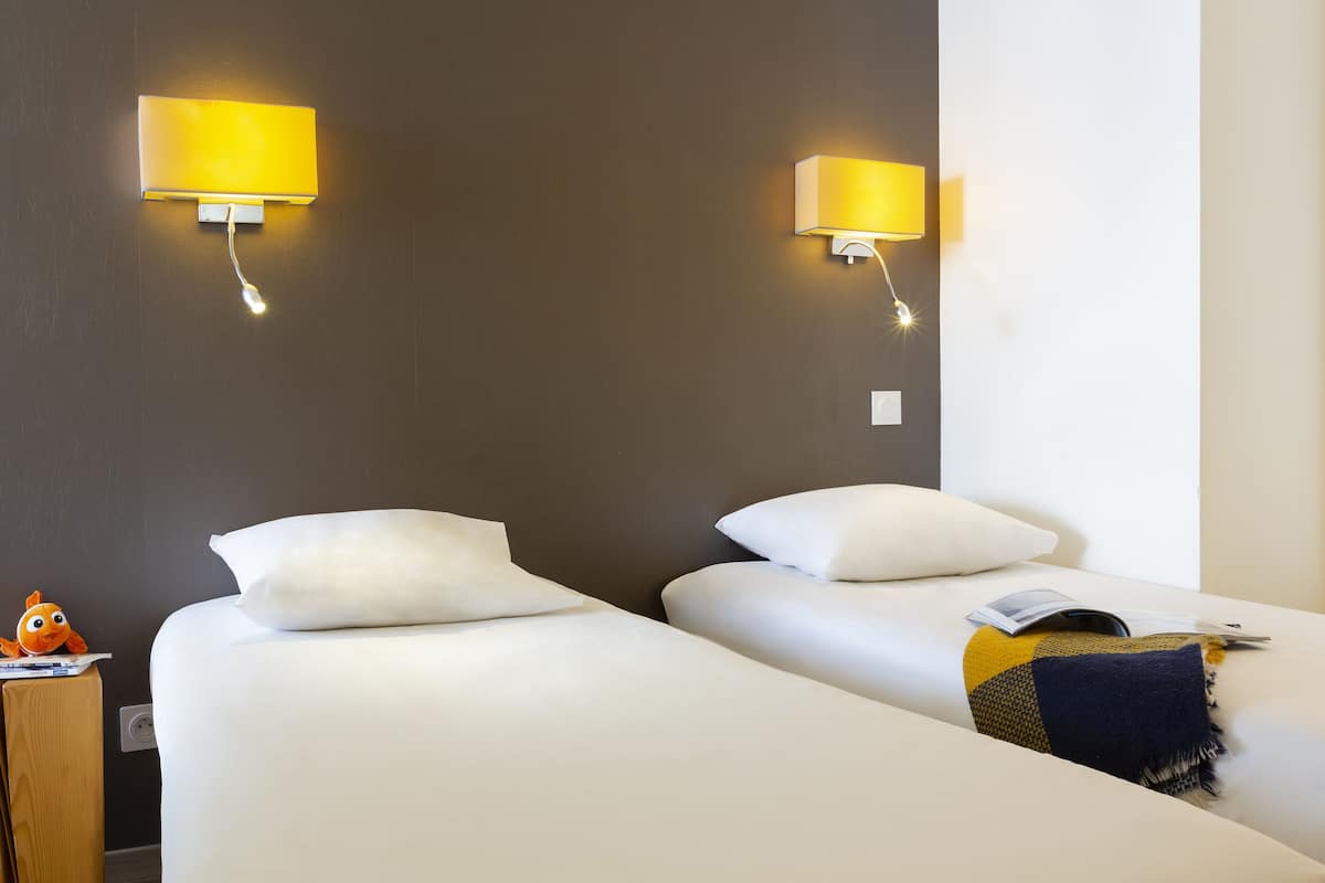 A hotel room with two beds, white bedding, a wooden nightstand with a fish figurine, and two wall-mounted lamps.