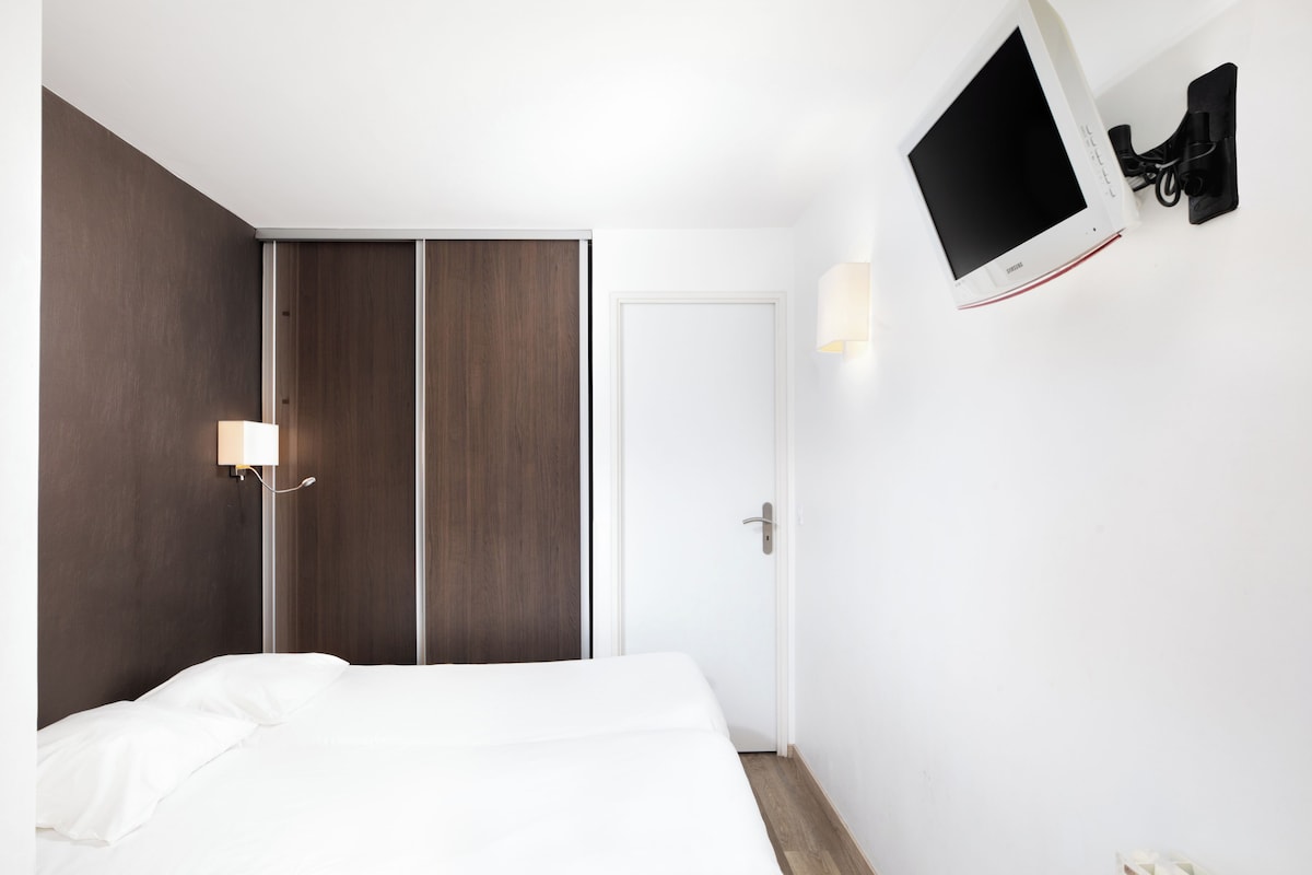 A hotel room with a bed, a wardrobe, a TV mounted on the wall, and a door.