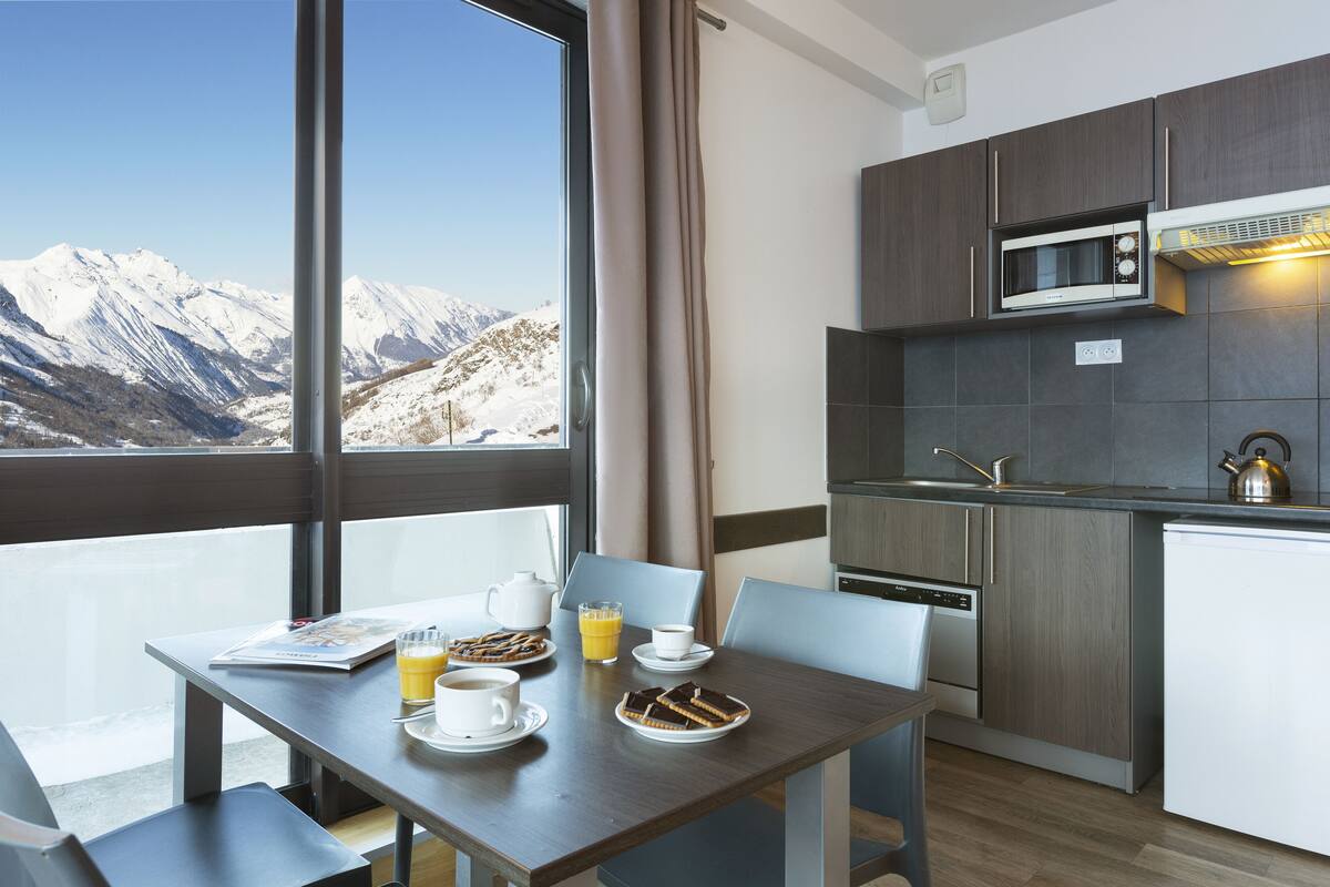 A modern kitchen with a view of snow-capped mountains, a dining table with breakfast items, and a built-in microwave.