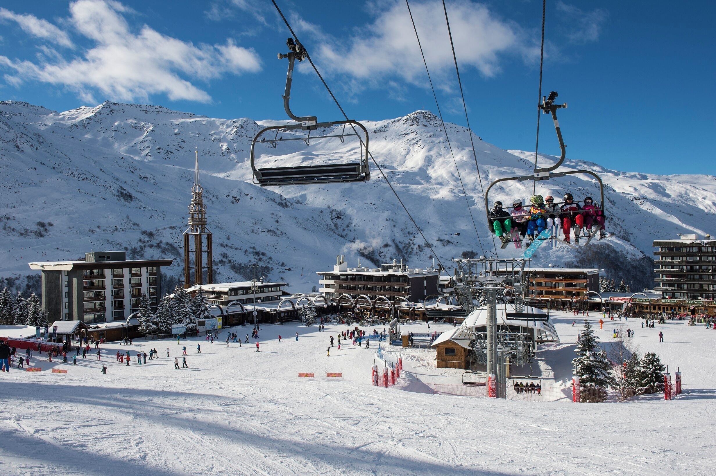Un centro de esquí con telesilla, laderas cubiertas de nieve y edificios al fondo.