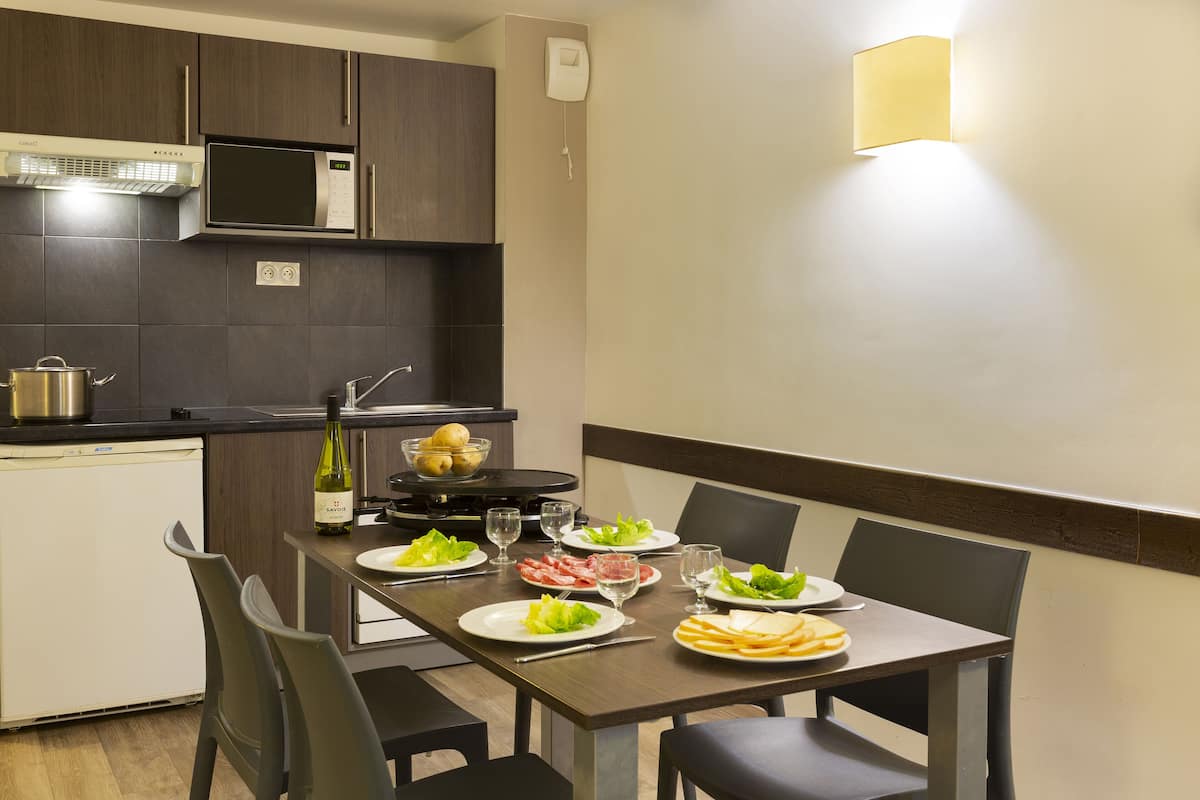 A modern kitchen with a dining table set for four, including plates of food, glasses, and a bottle of wine.