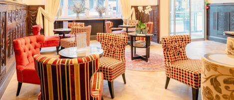 Un vestíbulo de hotel con un sillón tapizado rojo, sillas a rayas, una mesa redonda y una alfombra estampada.