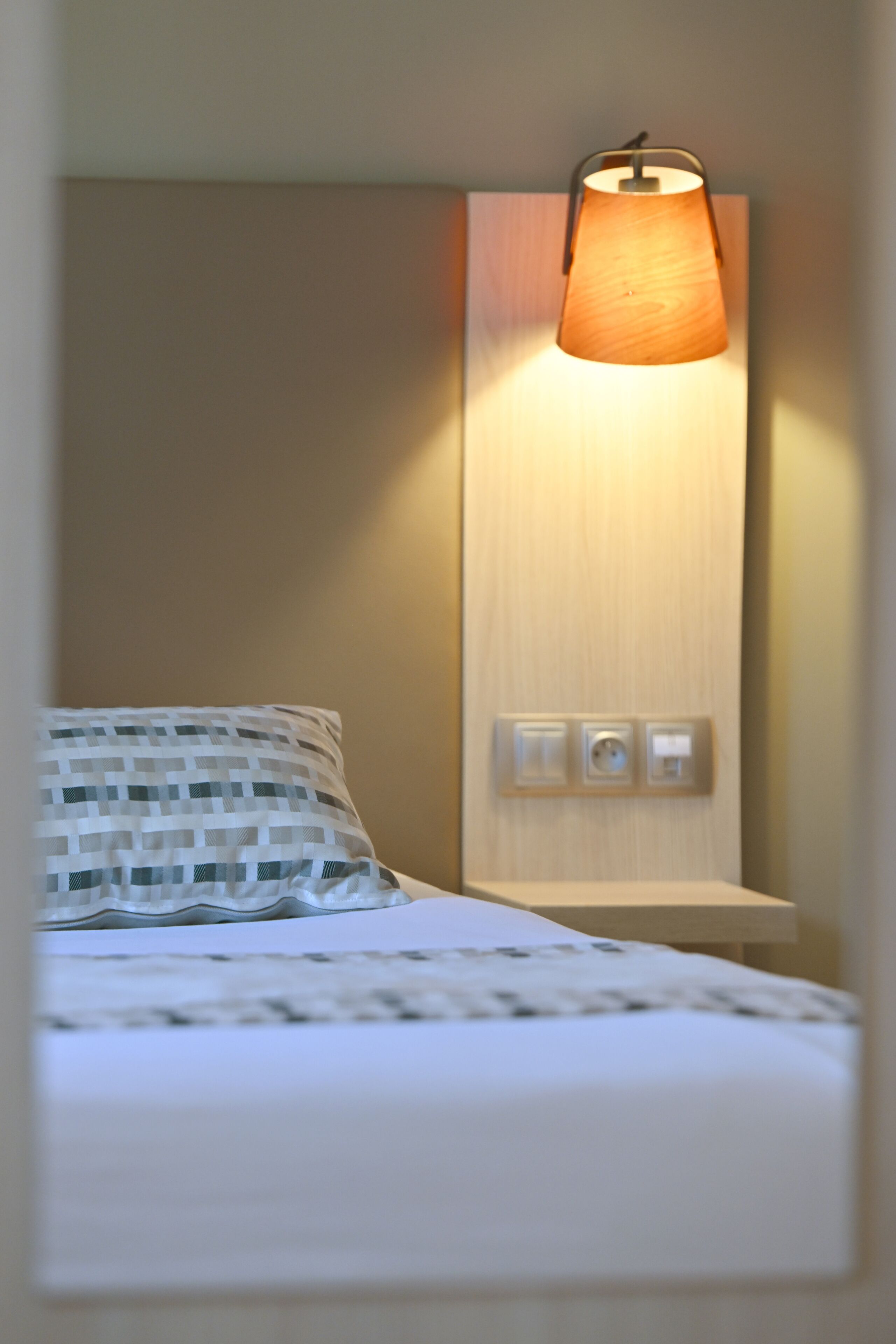 Un lit avec un oreiller à motifs, un luminaire fixé au mur et une prise de courant.