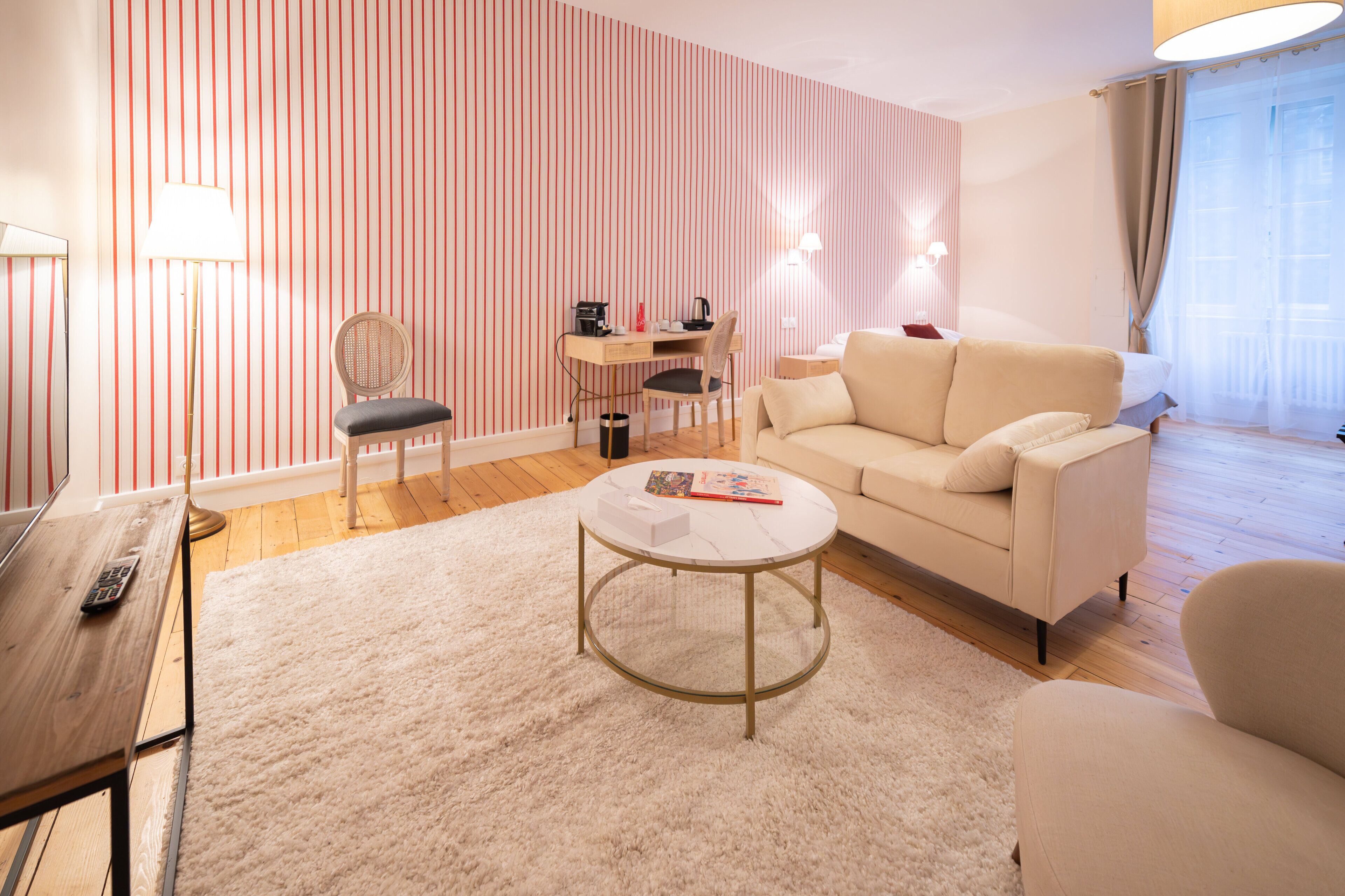 A modern living room with a striped wallpaper, a round coffee table, a sofa, a desk with a chair, and a lamp.