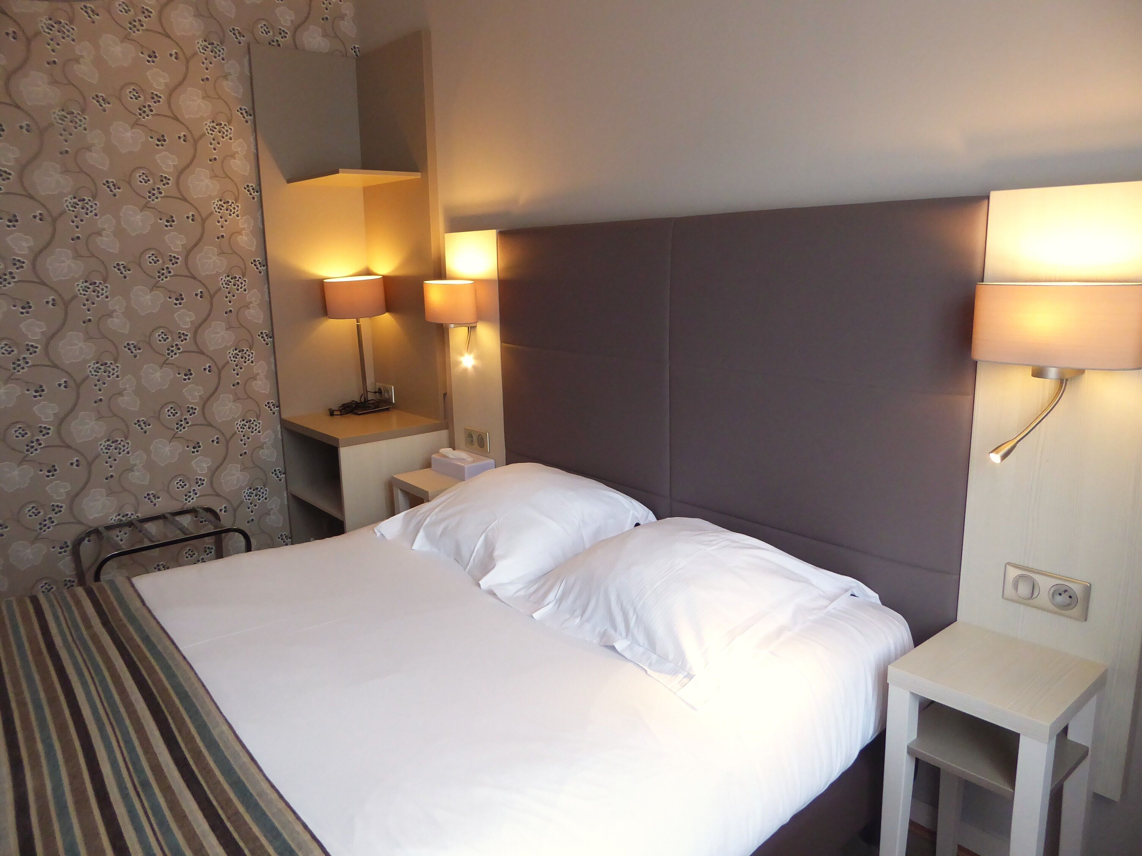 A hotel room with a large bed, two bedside lamps, a nightstand, and a striped blanket.