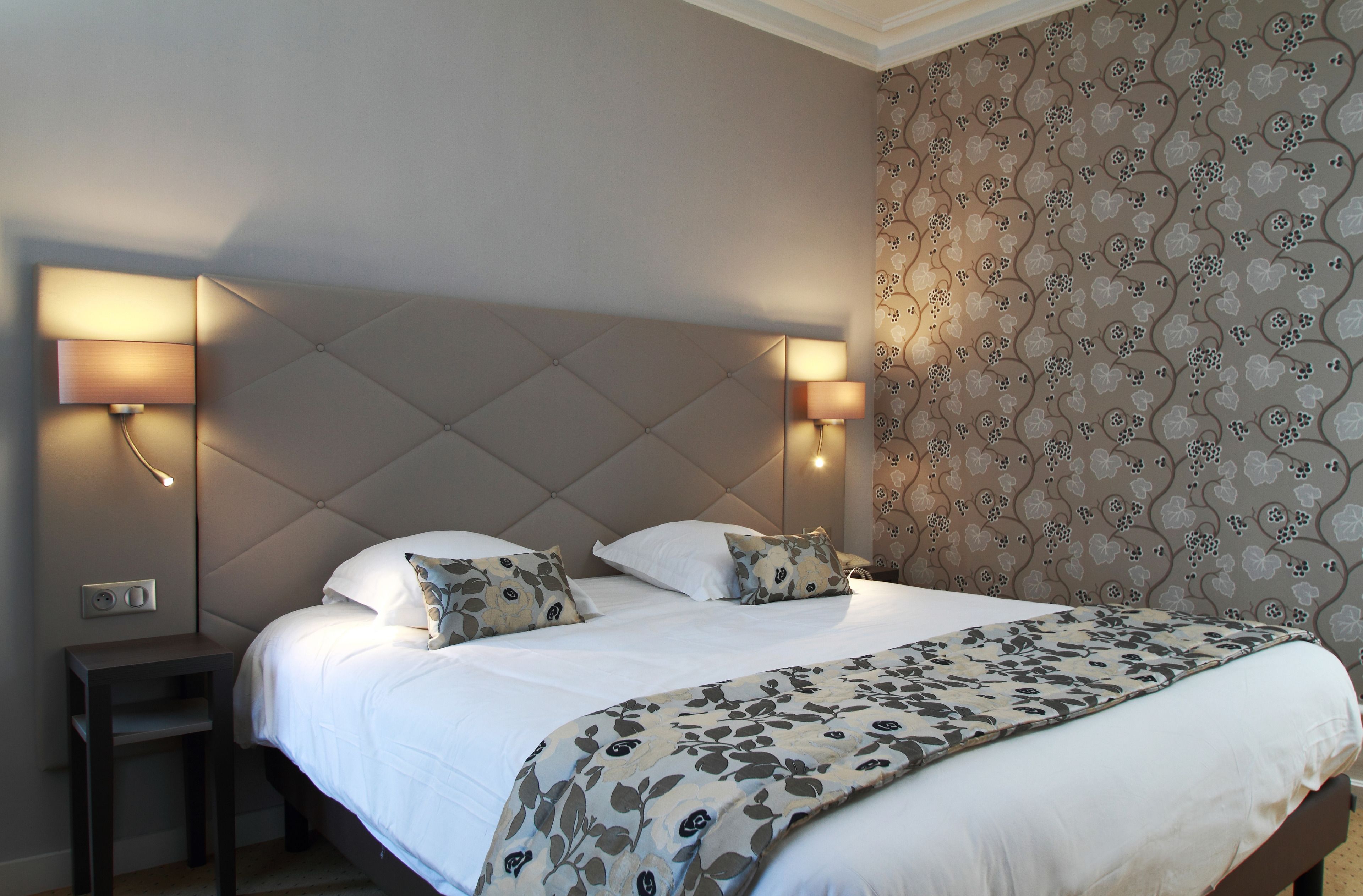 A hotel room with a large bed, two bedside lamps, a nightstand, and a floral-patterned wallpaper.