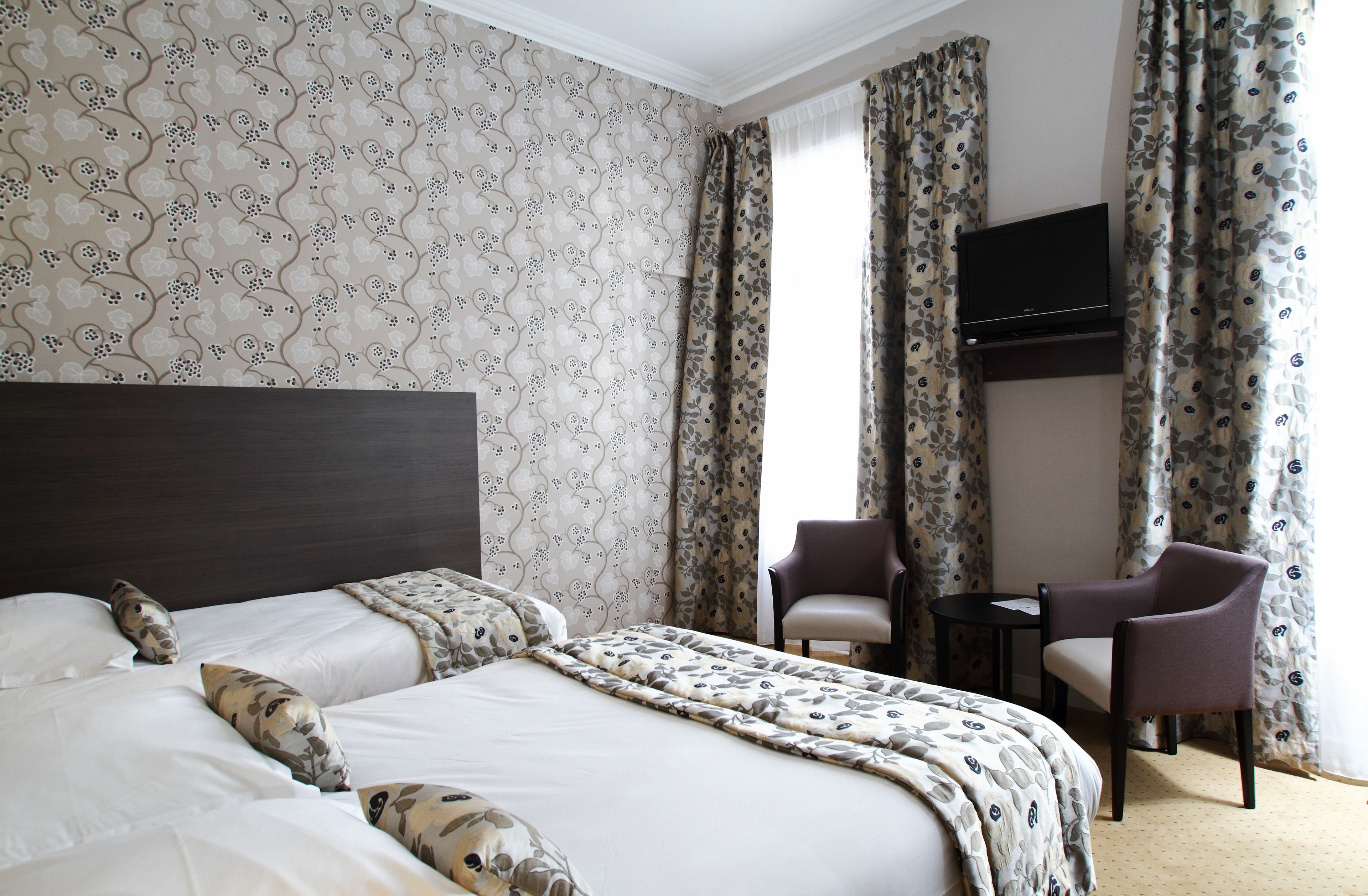 Una habitación de hotel con una cama grande, dos sillas, una mesita y un televisor fijado a la pared.