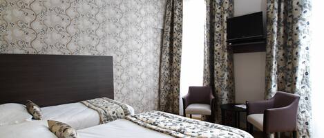 Una habitación de hotel con una cama grande, dos sillas, una mesita y un televisor fijado a la pared.