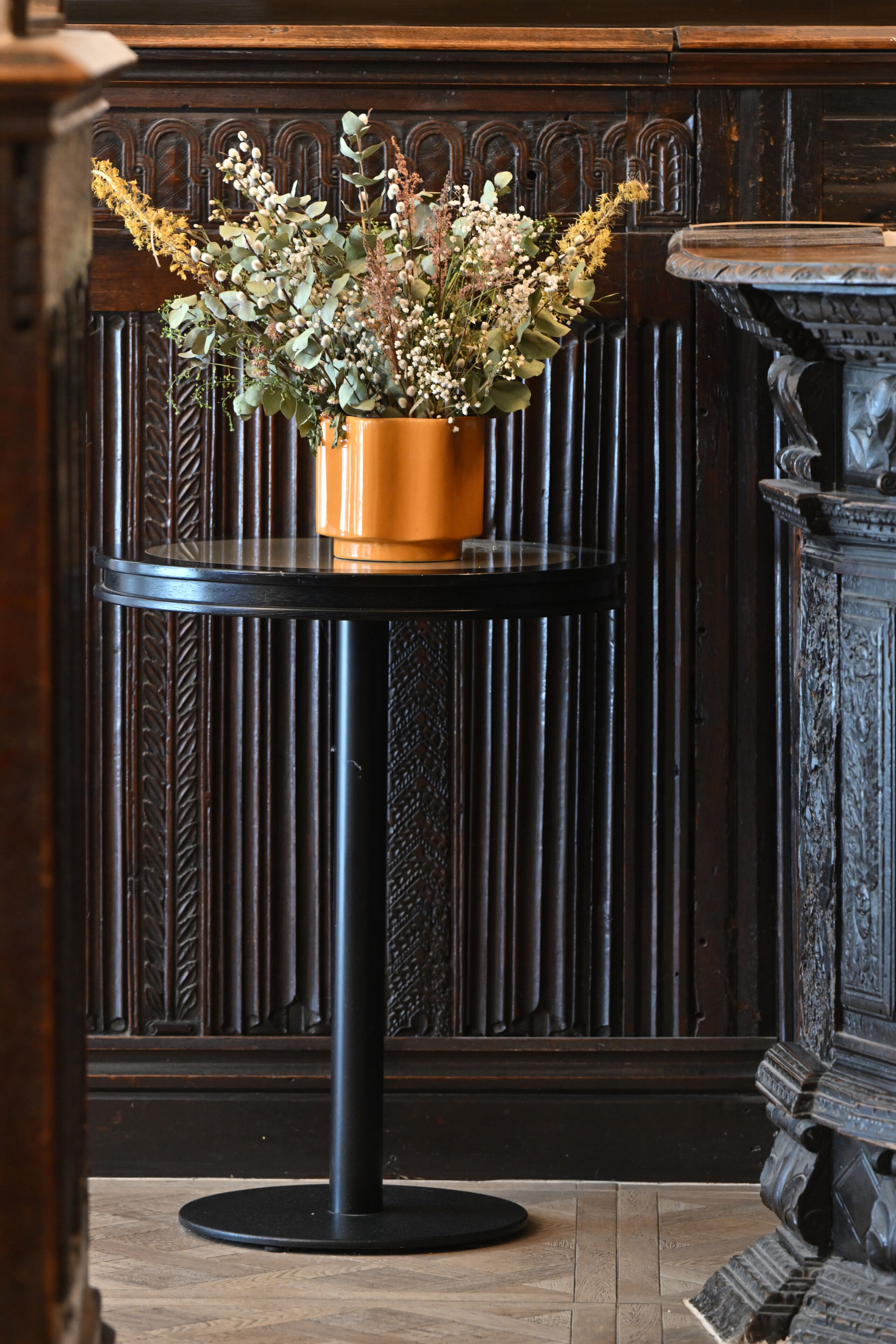 A table with a potted plant, a dark wooden backdrop, and a decorative urn.