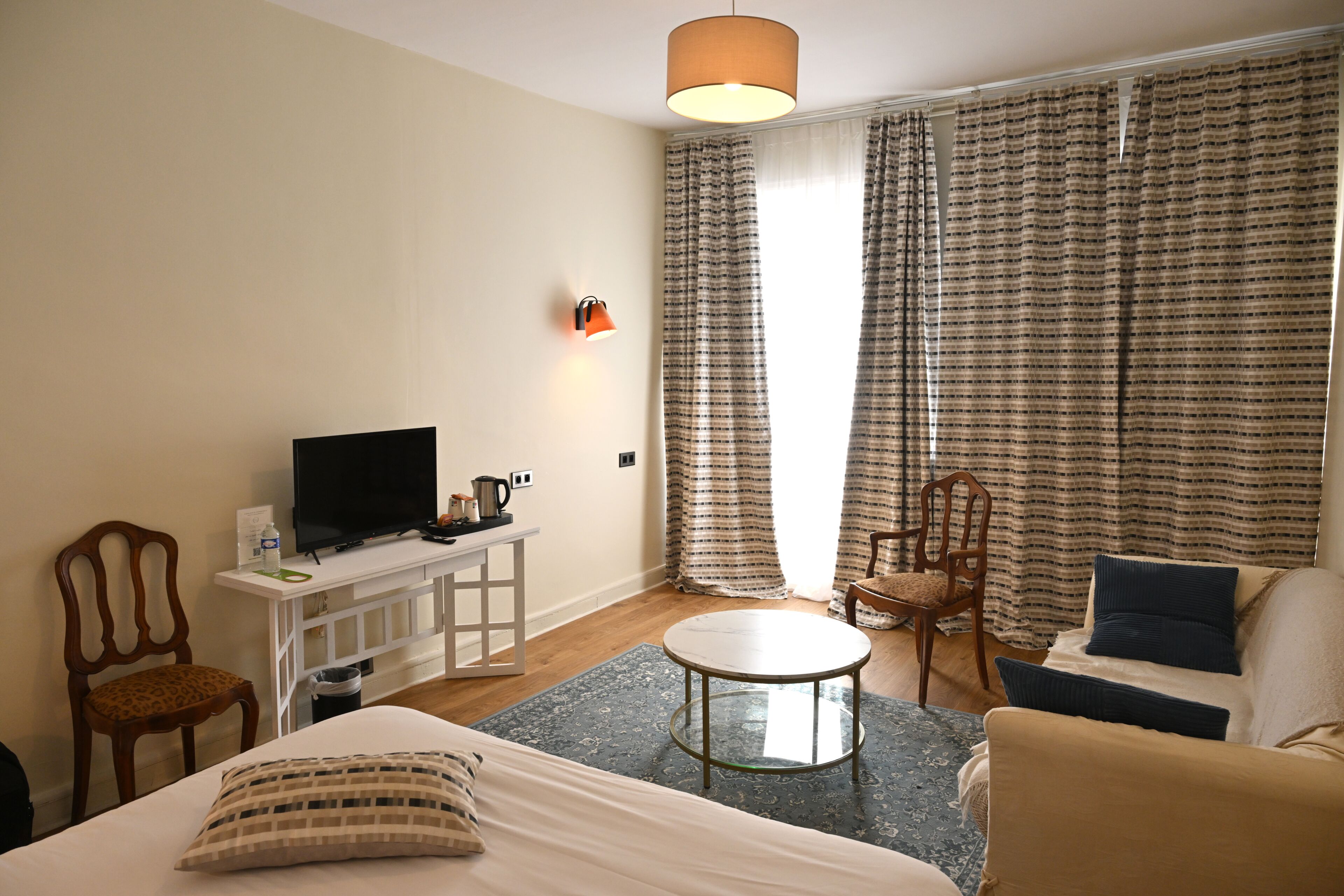 Quarto de hotel com uma cama, televisão, mesa pequena, sofá e cortinas.