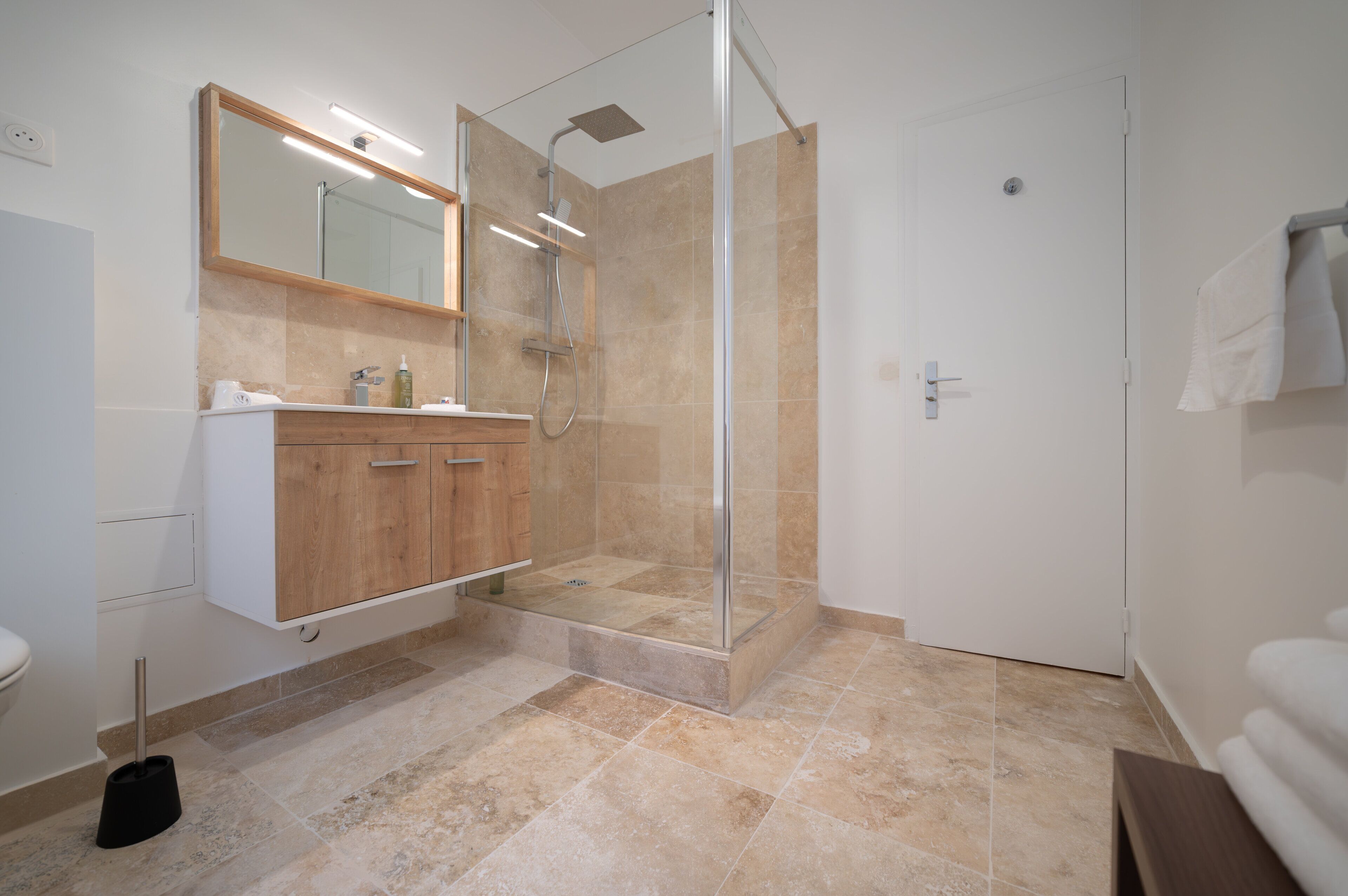 Un baño moderno con ducha de vidrio, tocador de madera y un espejo grande.