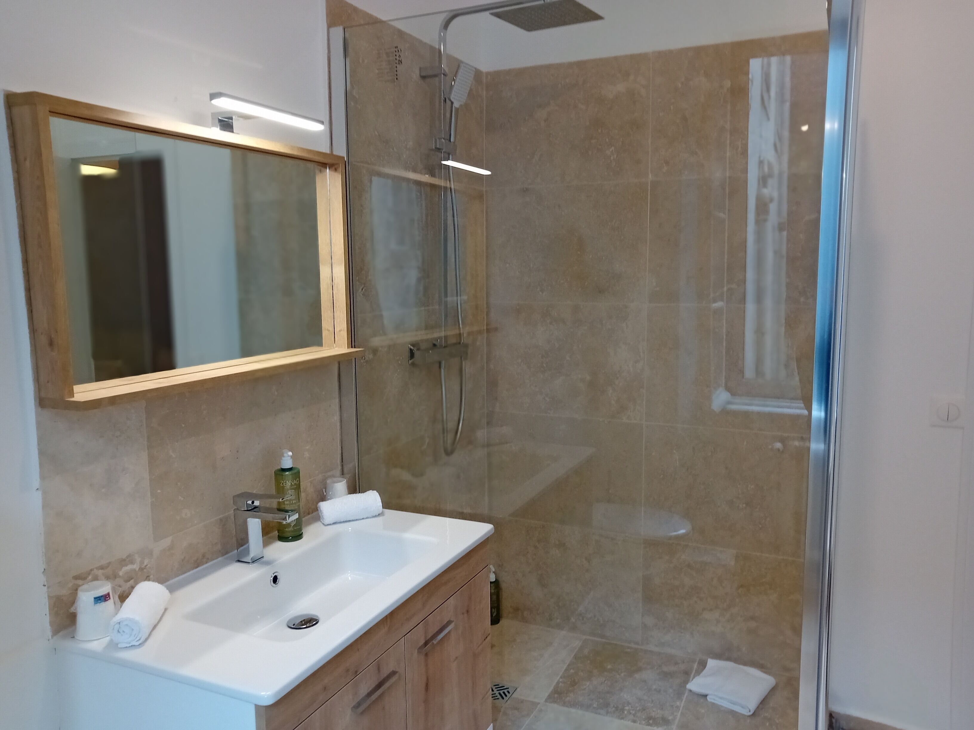 Un baño moderno con cabina de ducha de vidrio, un lavabo blanco y un espejo grande.