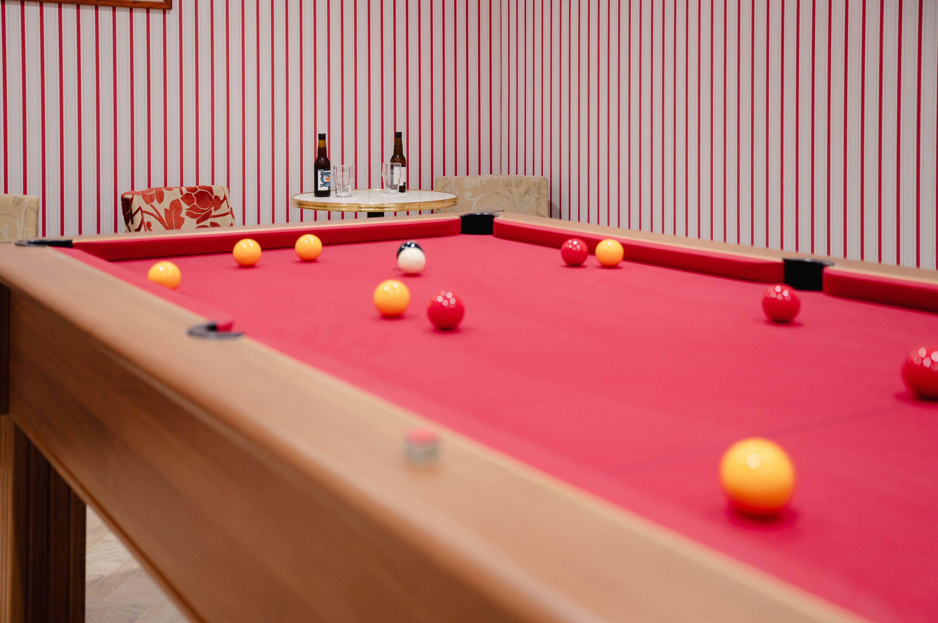 A pool table with balls and bottles, a cushioned chair, and a striped wall in the background.