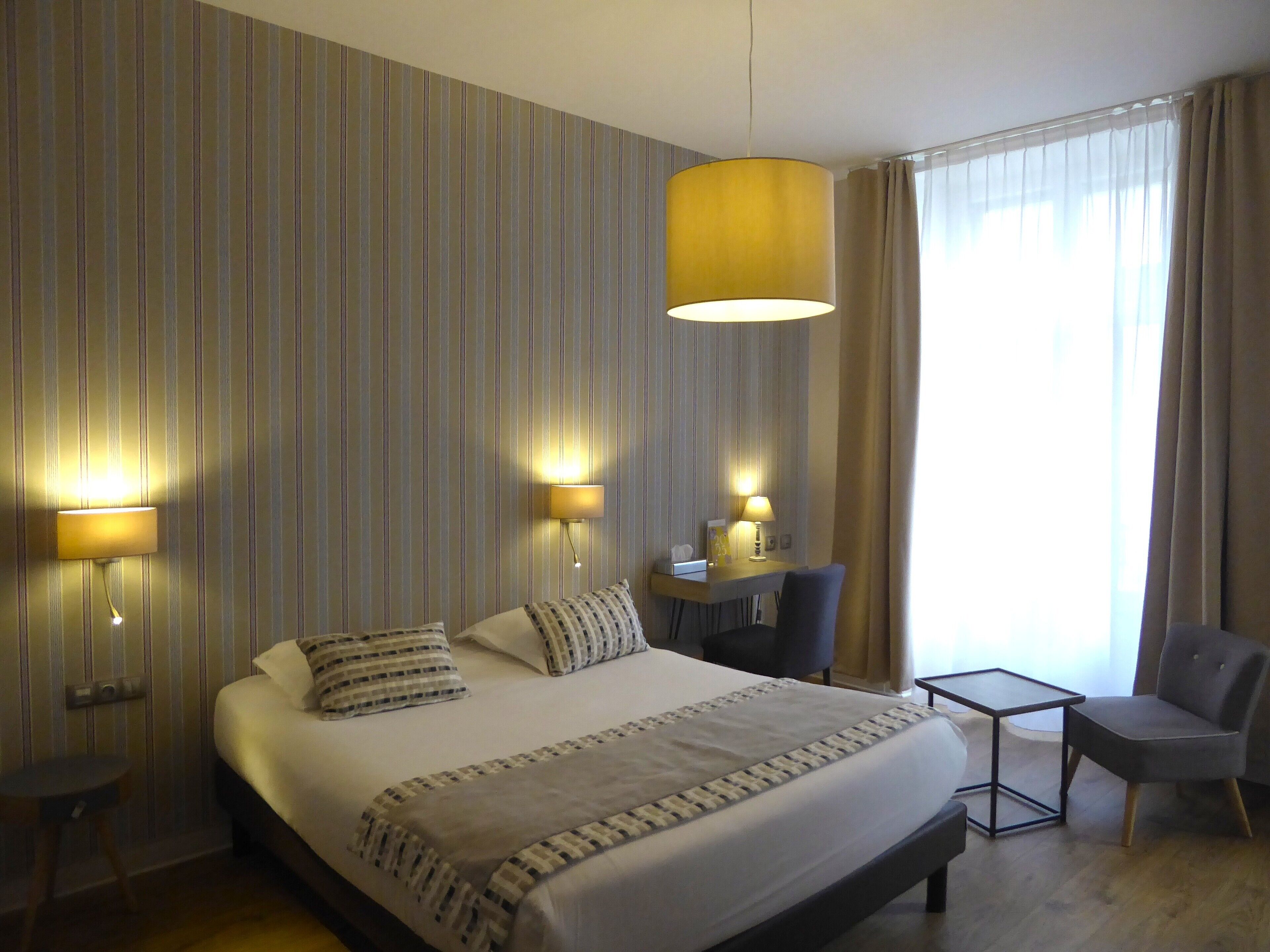 Une chambre d’hôtel avec un grand lit, deux lampes de chevet, un bureau avec une chaise et une fenêtre avec des rideaux.