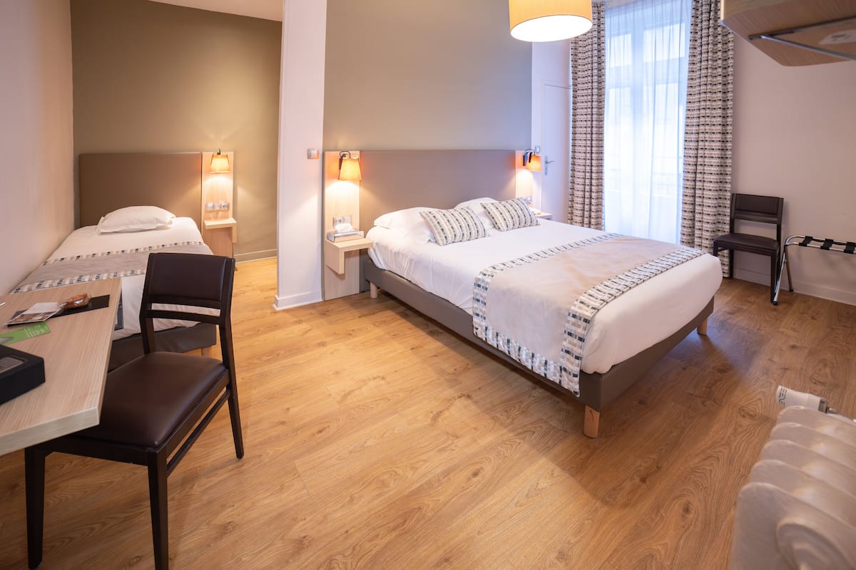 Une chambre d’hôtel comprenant un lit, des tables de chevet, un bureau avec une chaise et une fenêtre avec des rideaux.