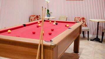 A pool table with balls, a chair, a small table with a vase, and striped wallpaper.