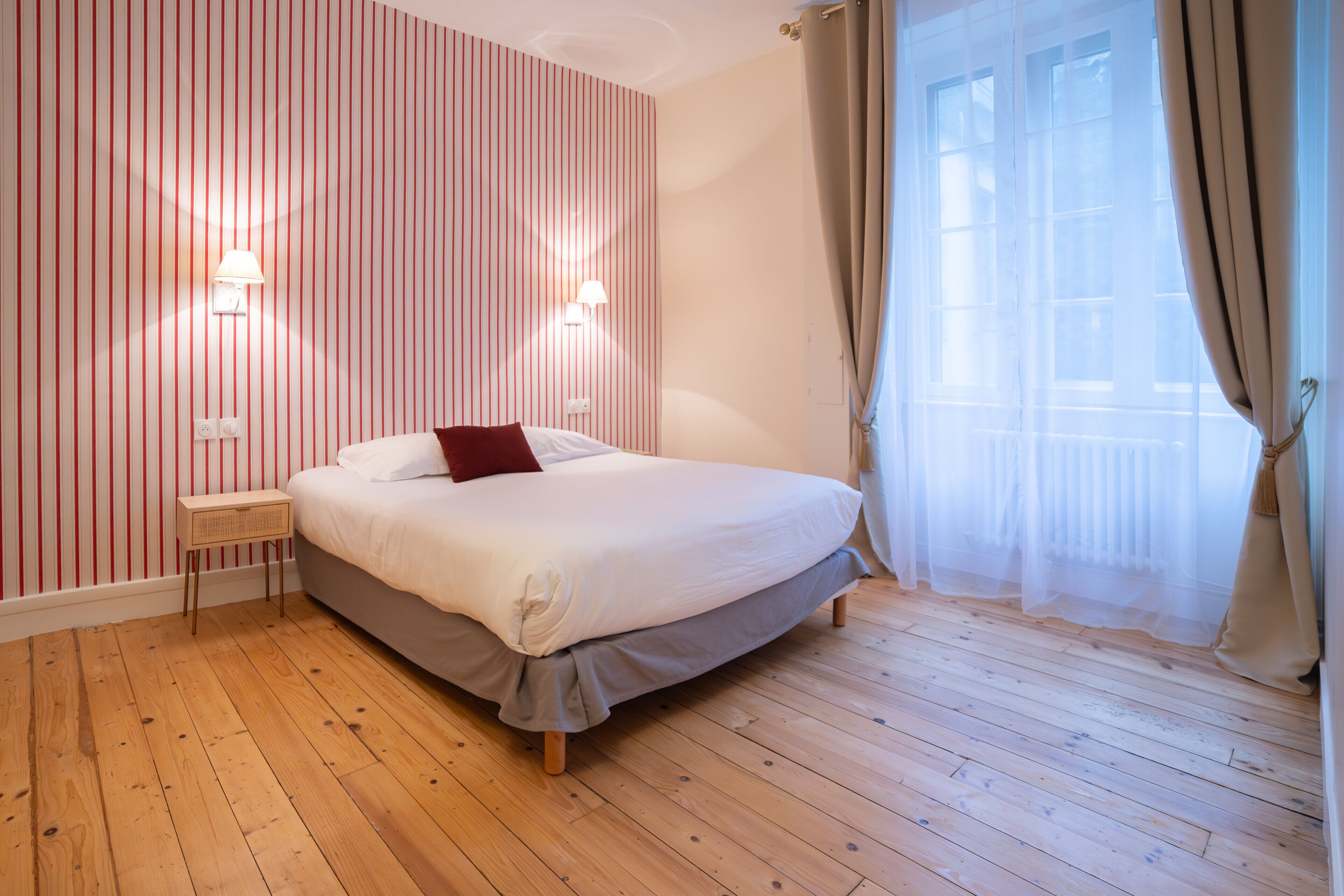 A bedroom with a bed, a bedside table, a lamp, and a window with curtains.