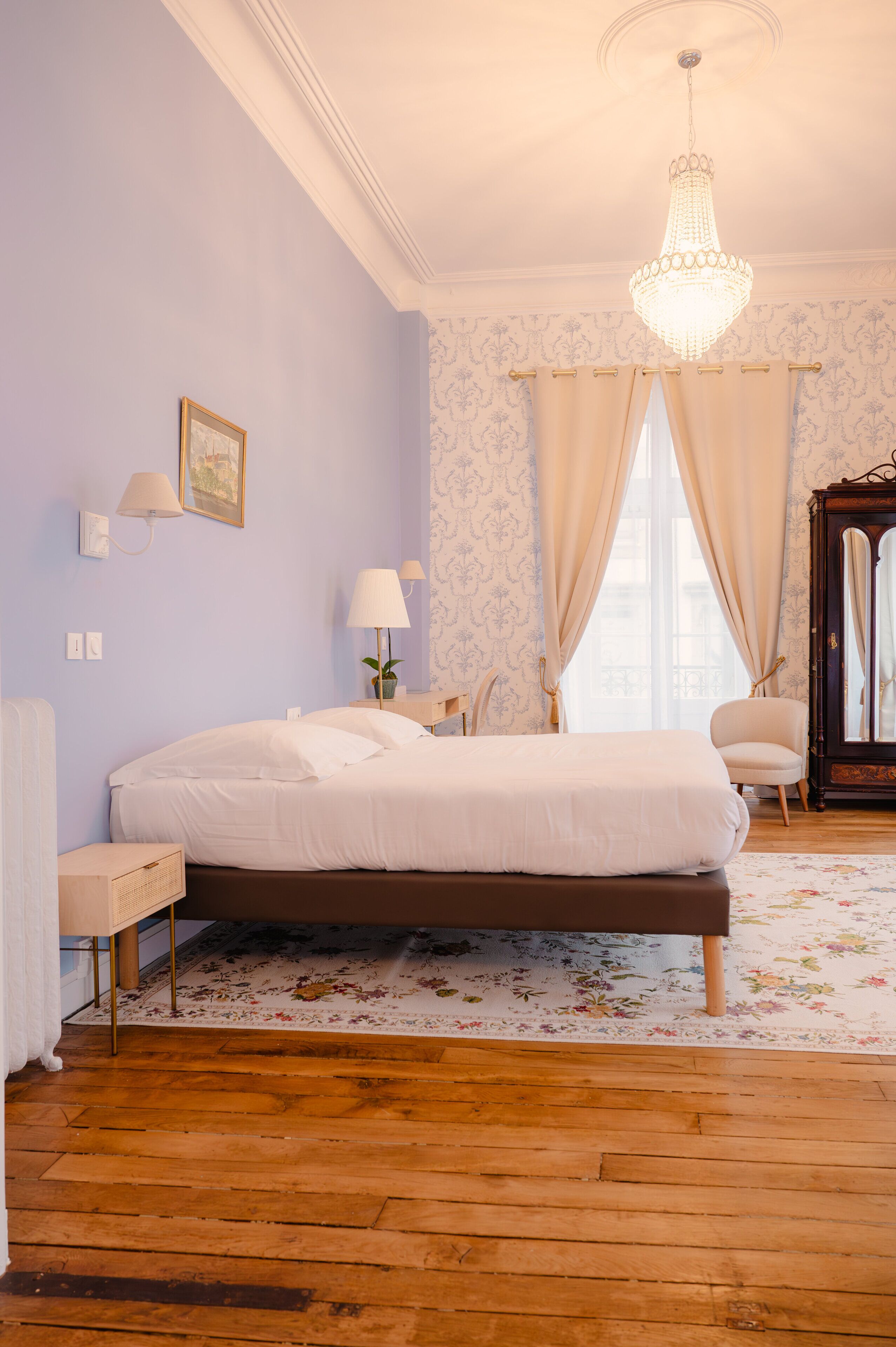 A bedroom with a bed, a nightstand, a chair, a dresser, a mirror, and a chandelier.