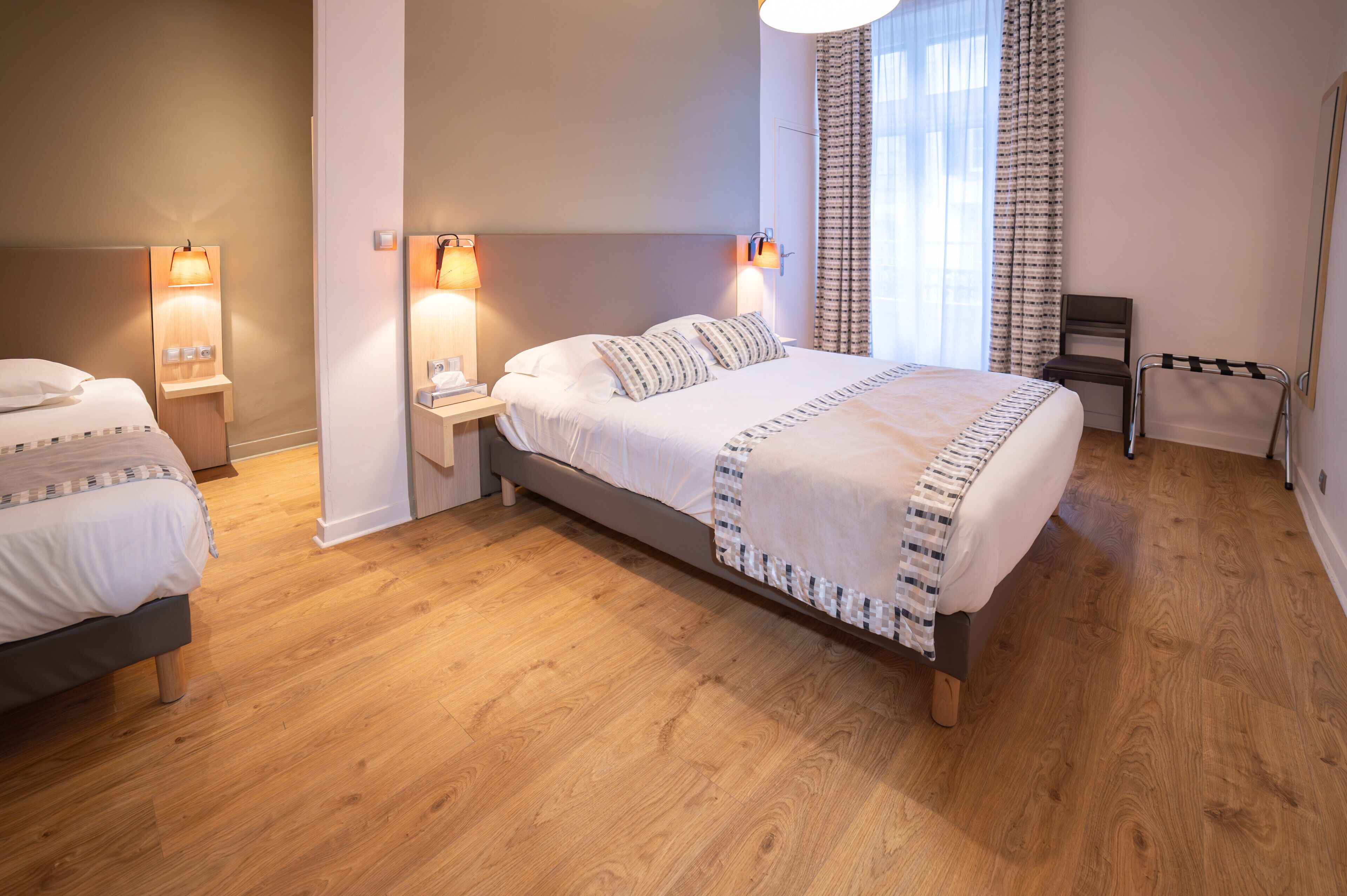 A modern hotel room with a large bed, bedside lamps, a chair, and a view of the city through the window.