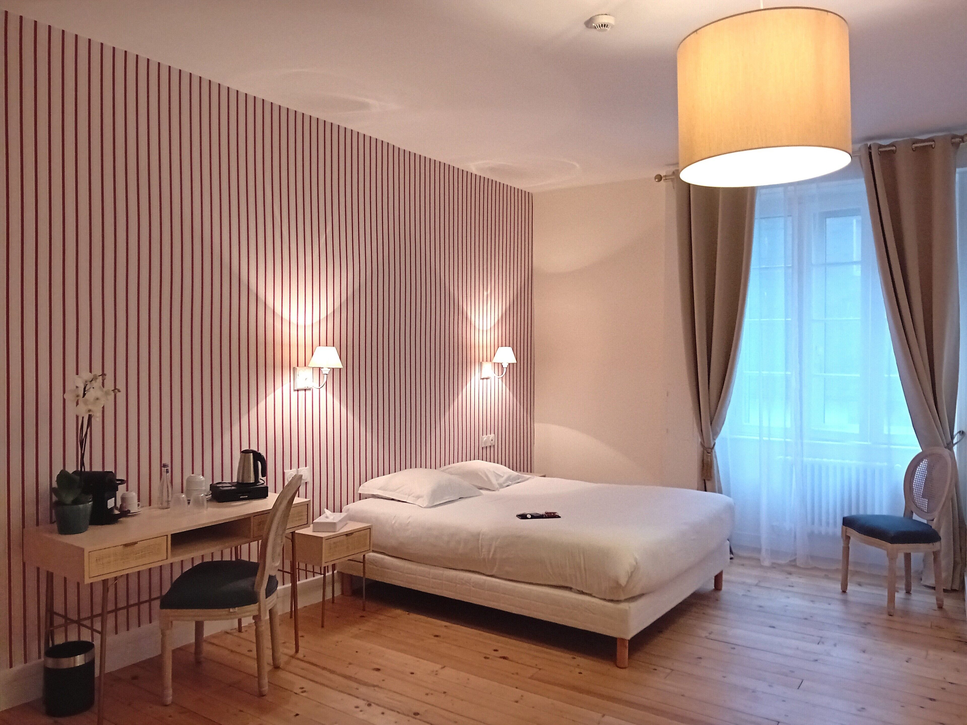 A hotel room with a bed, desk, chair, lamp, and curtains.